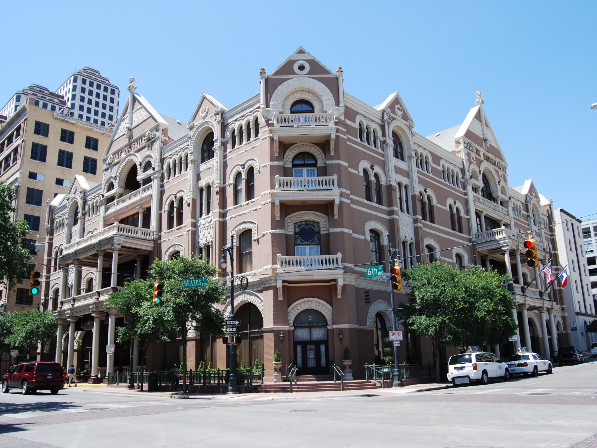 a close up of a busy city street. Historic hotel building. Person waiting to cross the street and people crossing the street.