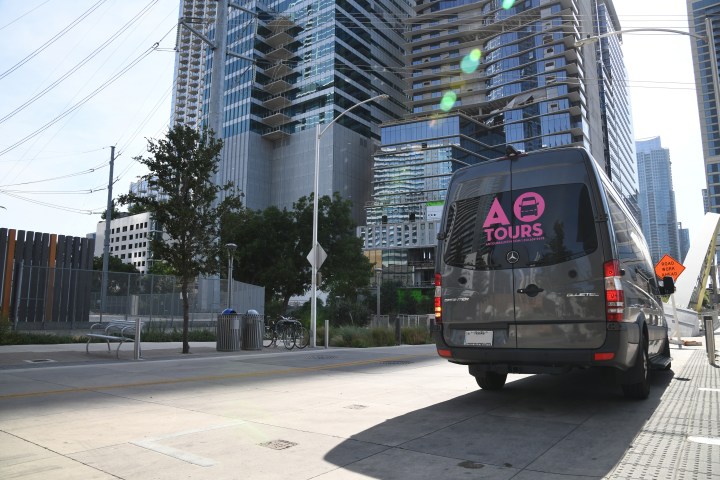 AO Tours Austin Gray bus parked near tall buildings in the street.