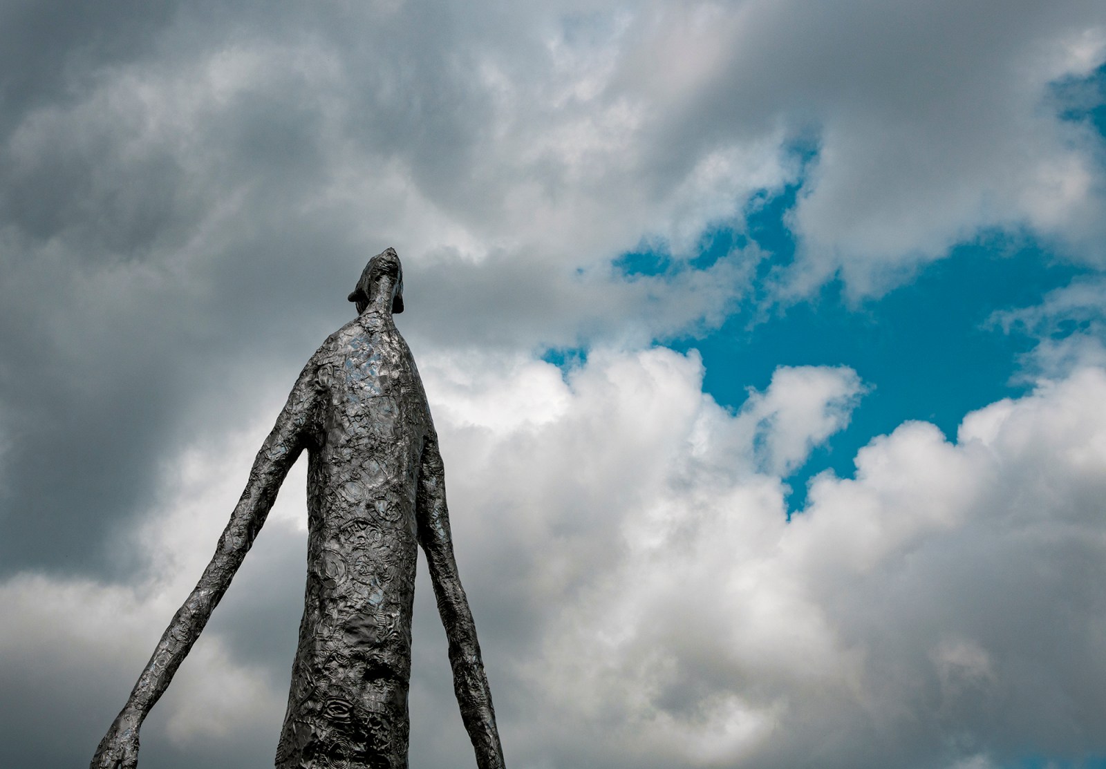 Metail sculputer that resembles tin fold of a long armed being looking up into the sky.