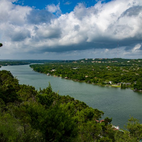View looking out over a river with lots of green trees and puffy white and gray clouds.
