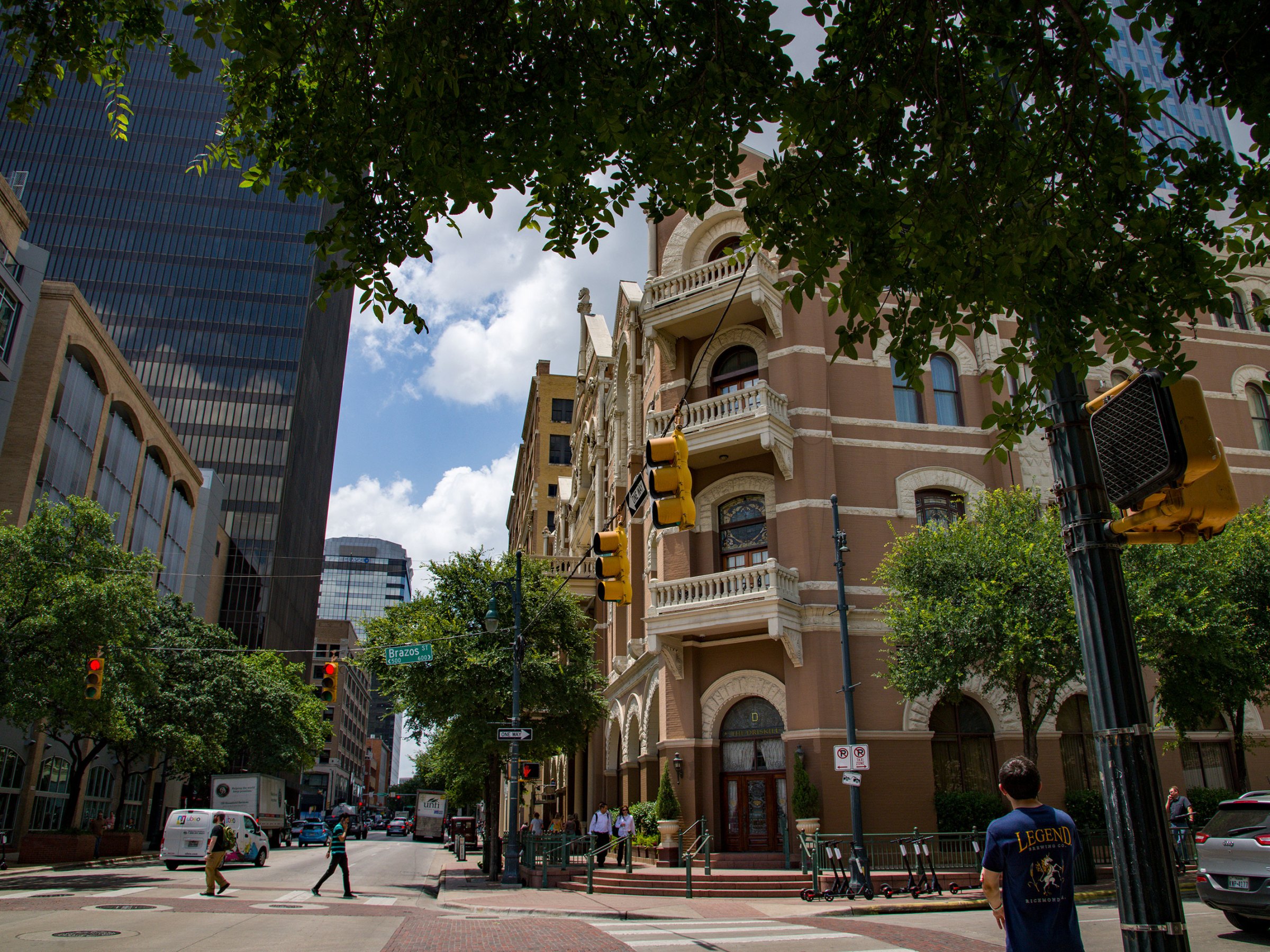 a close up of a busy city street. Historic hotel building. Person waiting to cross the street and people crossing the street.
