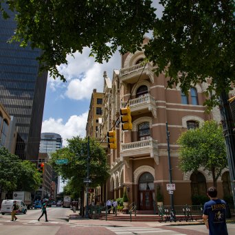a close up of a busy city street. Historic hotel building. Person waiting to cross the street and people crossing the street.