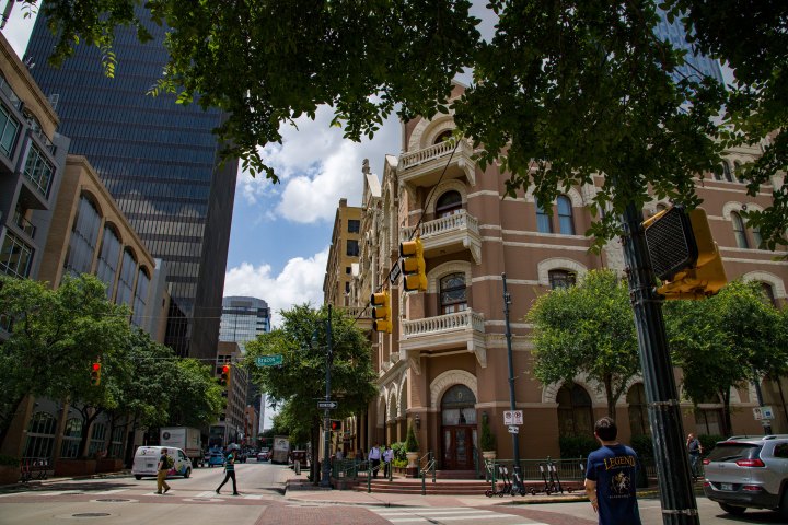 a close up of a busy city street. Historic hotel building. Person waiting to cross the street and people crossing the street.