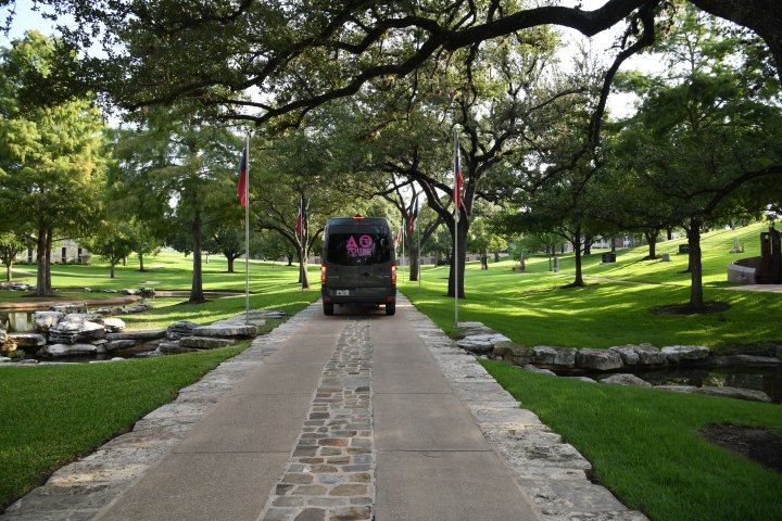 Dark Gray AO Tours Austin Sprinter Van on a small road with Texas Flags along the side