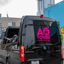 Street mural on side of a building with a horse and monopoly man character painted on it. Black AO Tours Austin Panoramic bus with pink AO Tours Austin logo on the back.