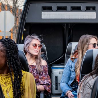 Passengers lauging and smiling on AO Tours Austin Panoramic Bus with the top down. Orange and gray fence on the left.