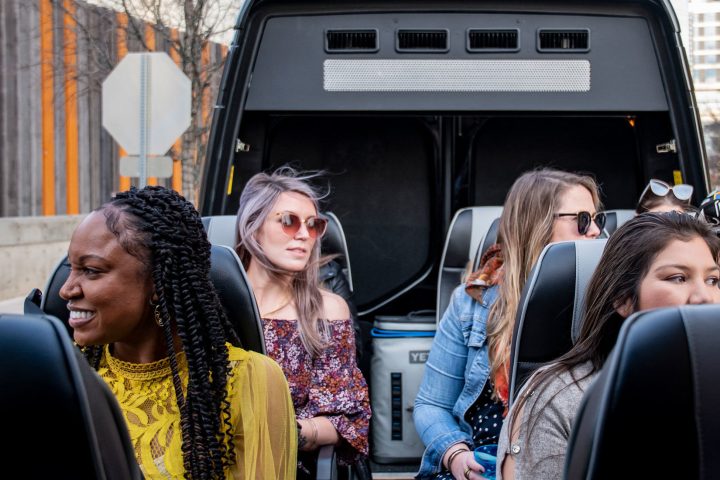 Passengers lauging and smiling on AO Tours Austin Panoramic Bus with the top down. Orange and gray fence on the left.