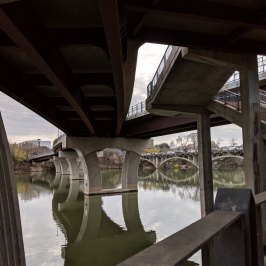 View of the underside of a pedestrian bridge with a river flowing under it.