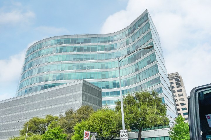 A tall glass building in a Austin, Tx. Trees growing up in front. Blue sky with white clouds.