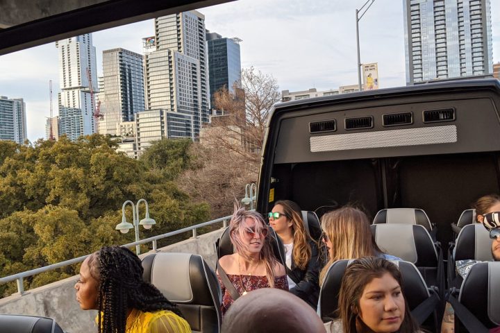 People sitting in panoramic bus with the top open. Austin skyline in the background.