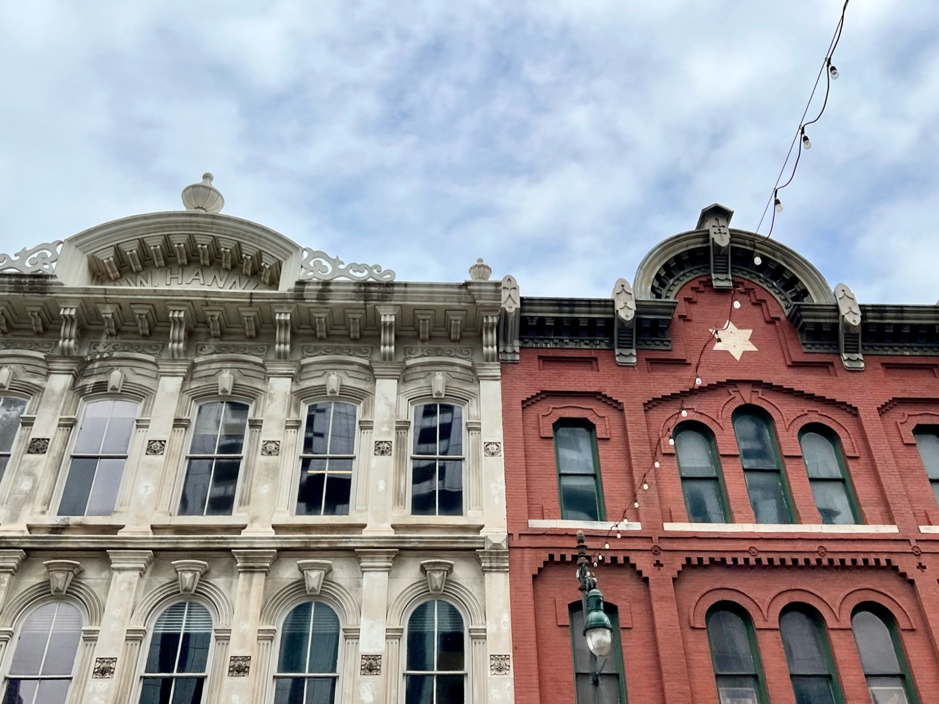 Historic building faces along East Sixth Street in Austin, Tx. One cream or white stone building and one brick red color building featuring a white star in the center of the top.