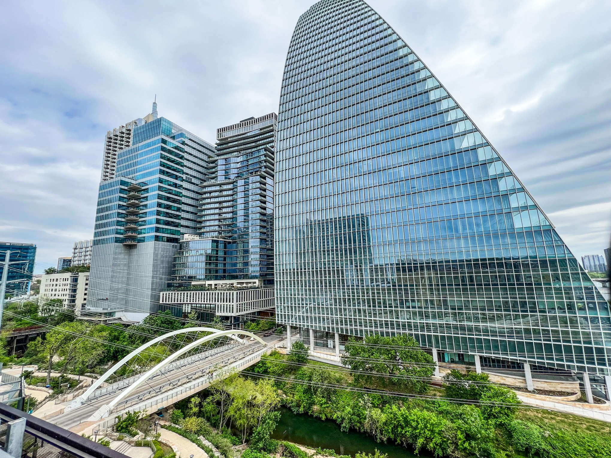 View of the butterfly bridge in Austin, TX from the Austin Central Library's roof top garden. Tall glass buildings, trees, overcast cloudy sky.