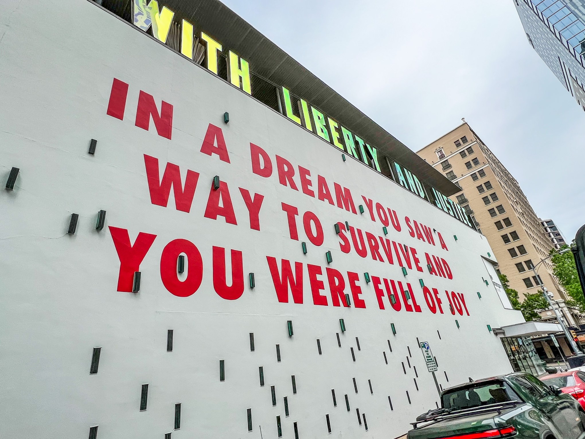 Large white wall on the outside of a building with large red letters painted on the side that say, 