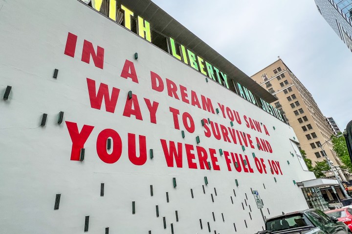 Large white wall on the outside of a building with large red letters painted on the side that say, 