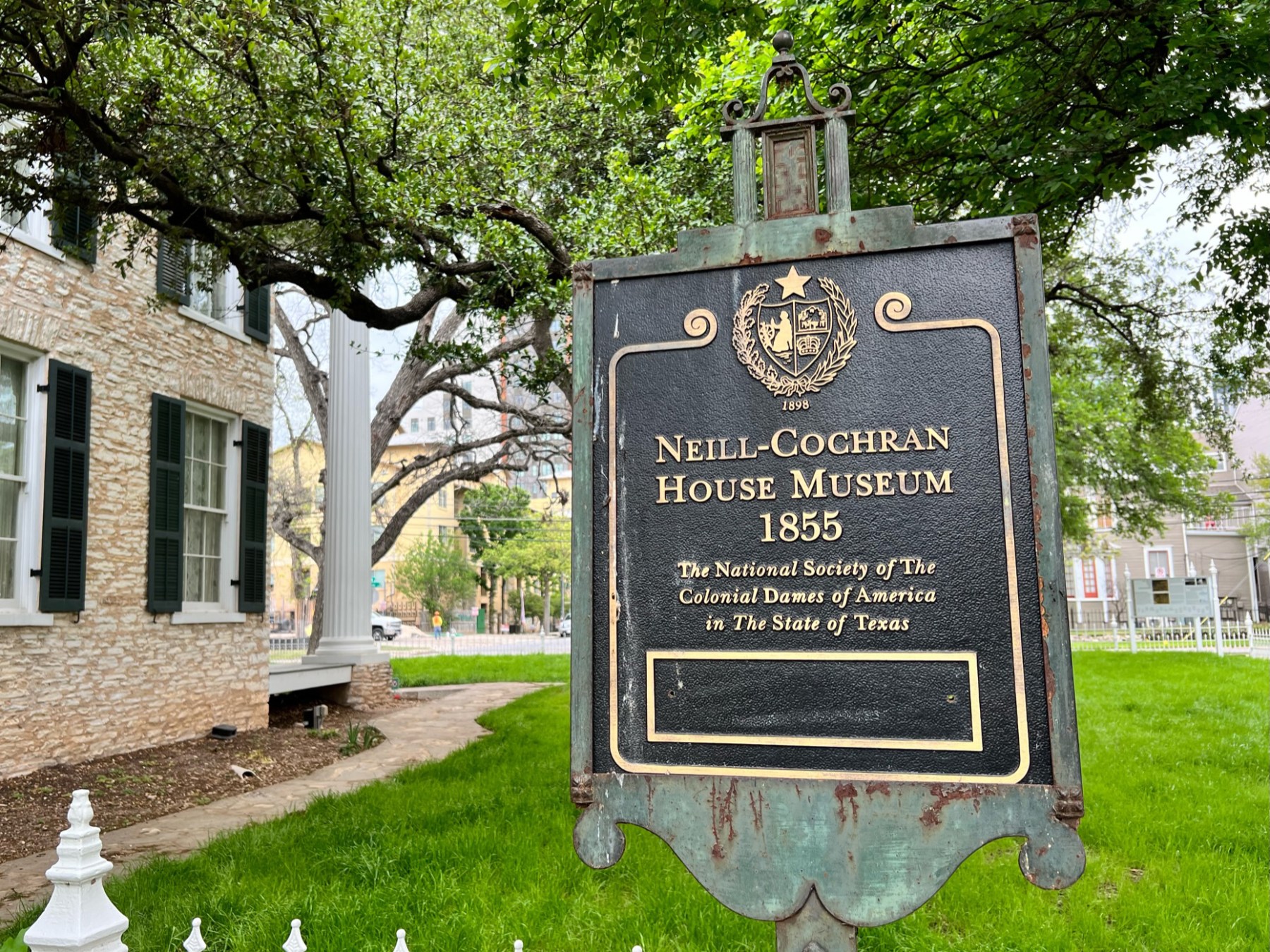 Neill-Cochran House Museum. A large brick historic house with a sign in the front yard. White iron fence, green grass lawn, heritage trees in the background.