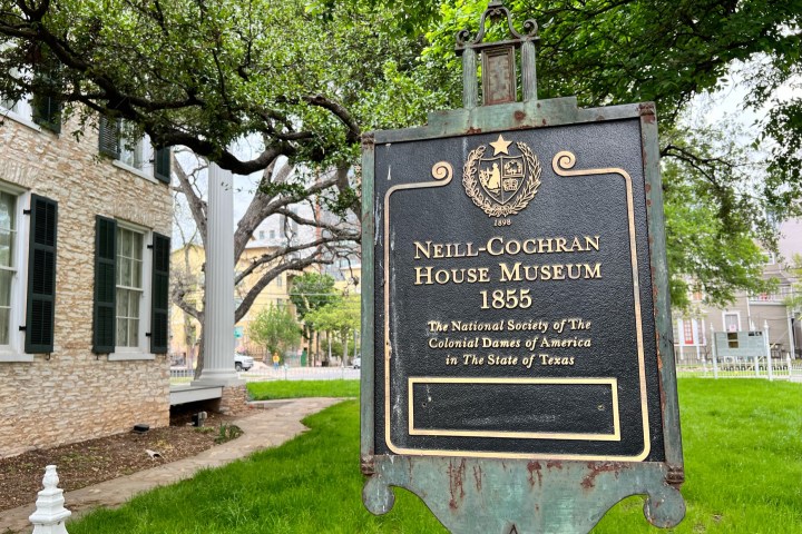 Neill-Cochran House Museum. A large brick historic house with a sign in the front yard. White iron fence, green grass lawn, heritage trees in the background.