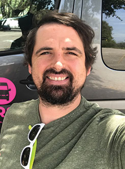Joel a man smiling for the camera in front of AO Tour Austin Bus