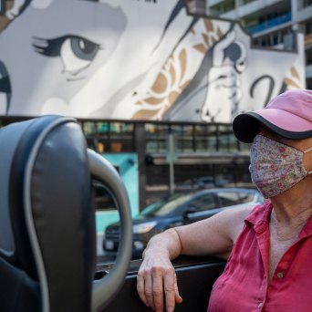 a person wearing a pink hat sitting in AO Tours Austin Panoramic Bus with face mural in the background