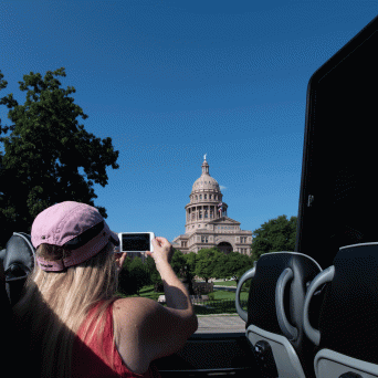 Blond woman with pink hat taking a photo of the Texas Capitol